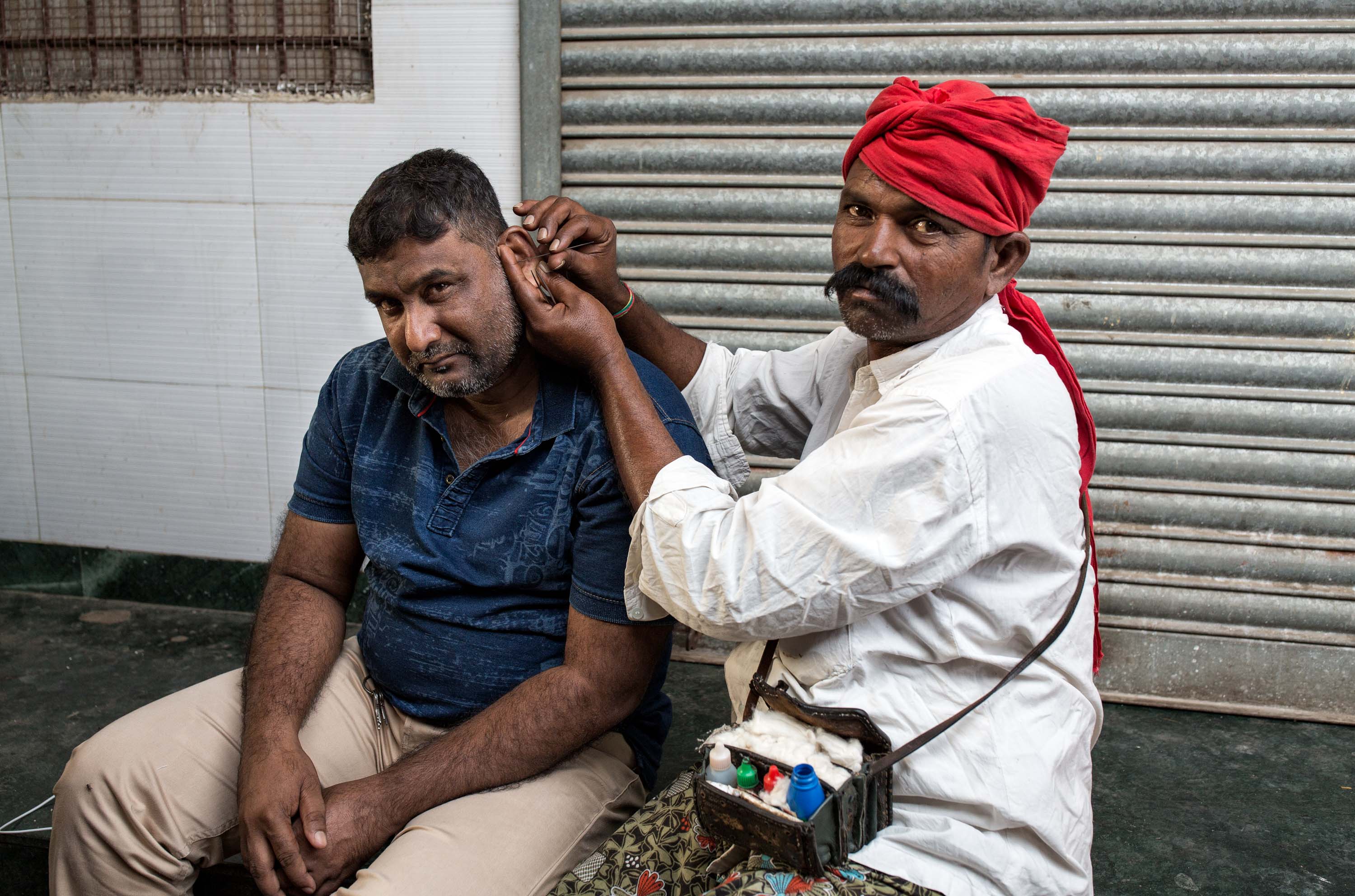 Professional ear cleaner, works on a customer on a street in Mumbai, India.
